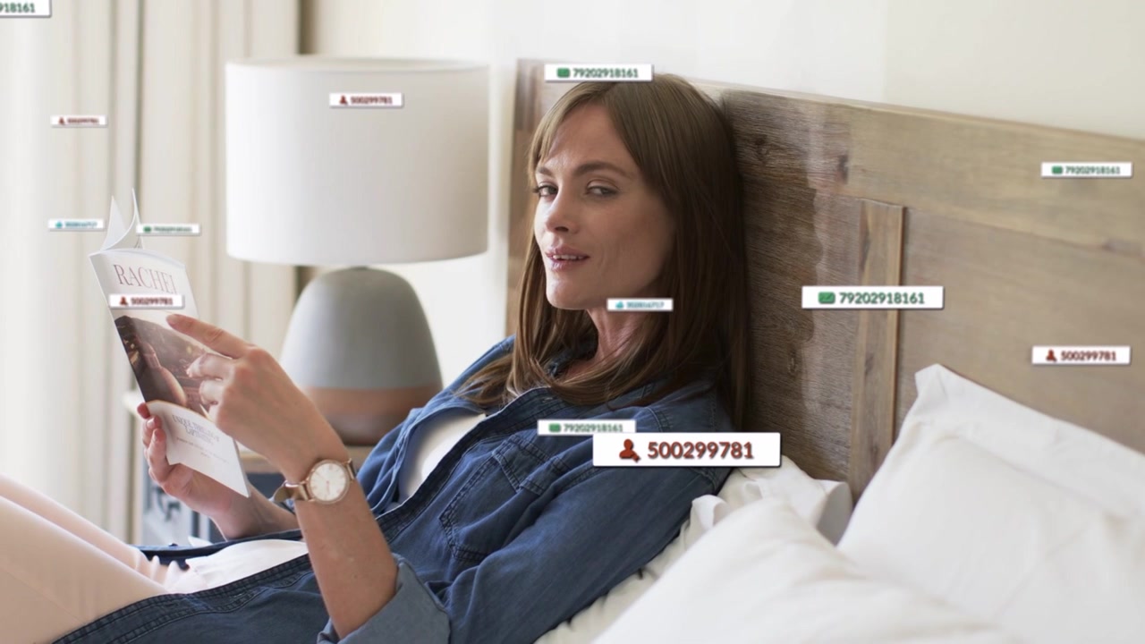 Woman lying on bed reading mag, labels appearing around her, moving, shifting gaze to camera tech