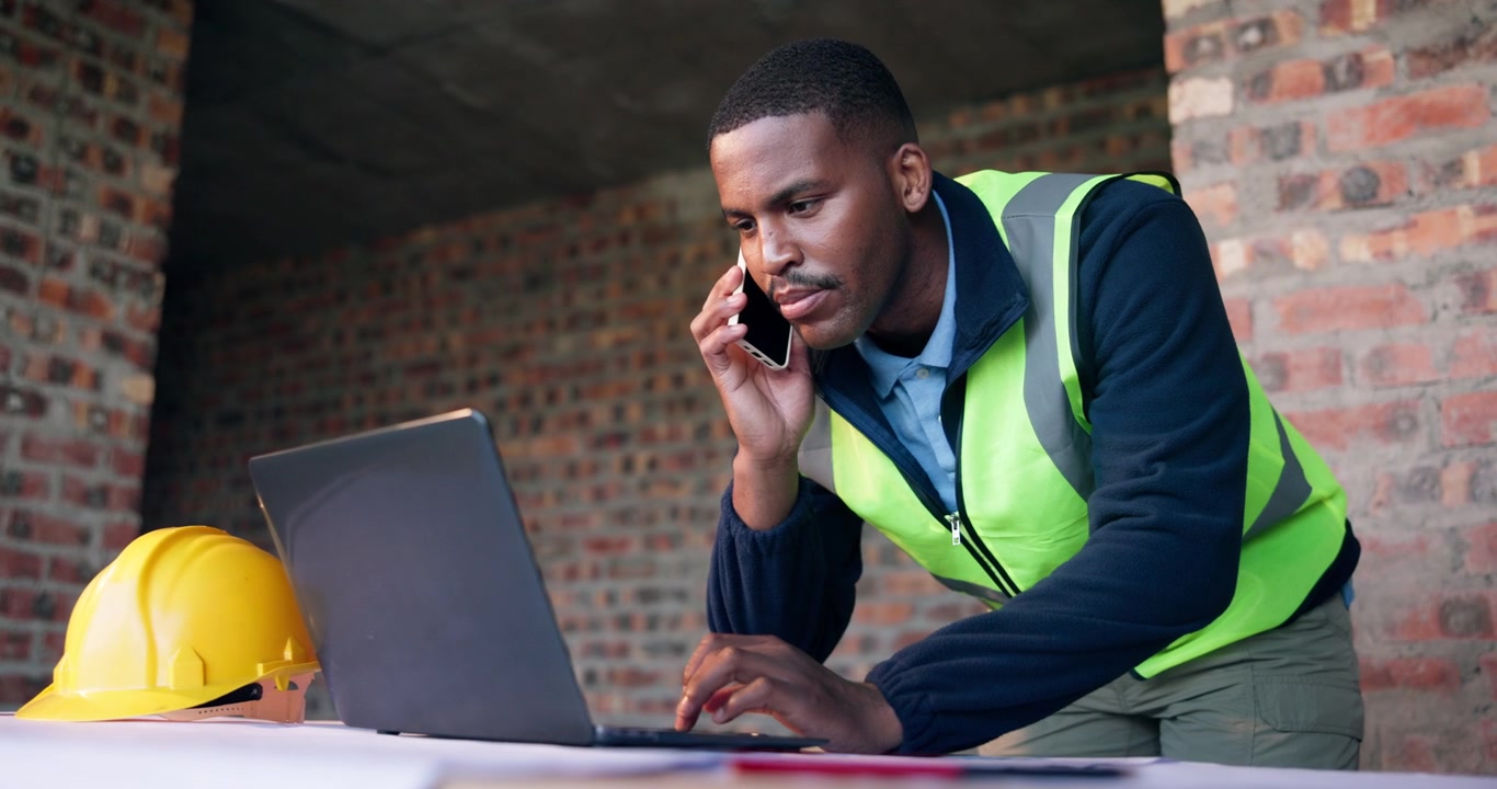 Construction Manager Talking on Phone and Using Laptop at Building Site