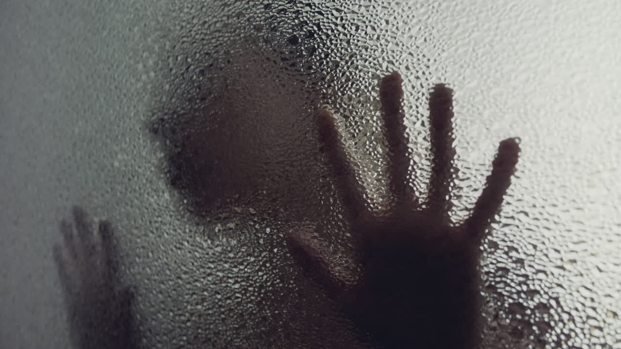 A female silhouette behind the frosted window touches the glass slowly