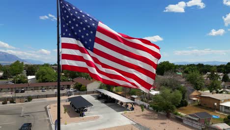 Amerikanische-Flagge-Weht-Im-Wind-An-Einem-Schönen-Sonnigen-Sommertag-Mit-Wolken-Und-Blauem-Himmel-Mit-Blick-Auf-Die-Berge.-Drohne-Schwenkt-Langsam-Im-Uhrzeigersinn-Um-Den-Fahnenmast-–-In-4K-60fps