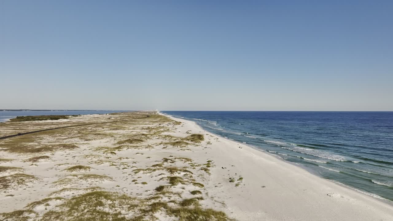 Aerial pan drone shot of the tip of Pensacola Beach, capturing the expansive coastline, surrounding waters and clear blue sky in a sweeping aerial view