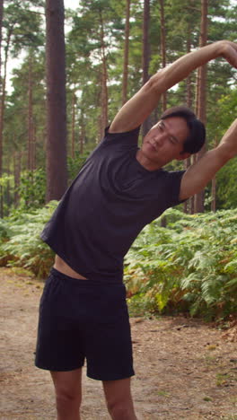 vertical video of man warming up and stretching before work out exercising running through forest shot in real time