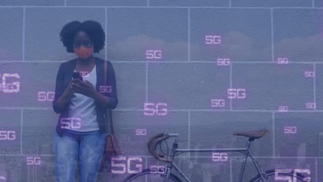 animation of 5g text banners over african american woman wearing face mask using smartphone
