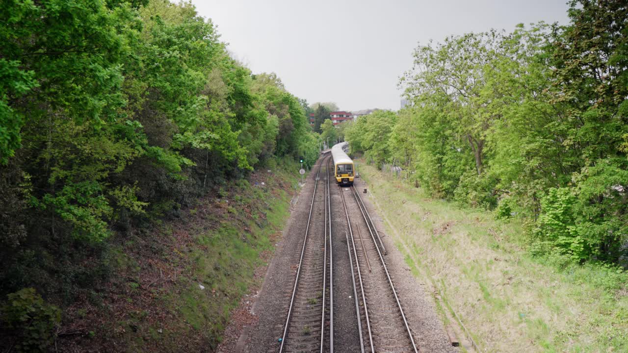 High angle view of a train taking off from a station and coming towards the camera between green trees and beautiful nature forest during daytime