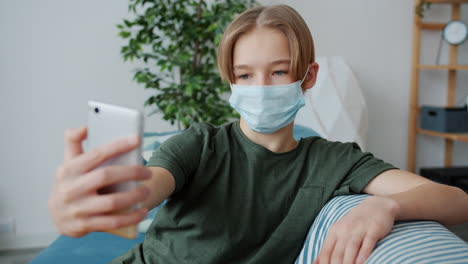 Teenager Wearing a Mask Takes a Selfie on Smartphone at Home