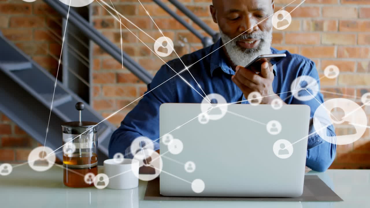 Animation of connected icons over african american man talking on cellphone and working on laptop