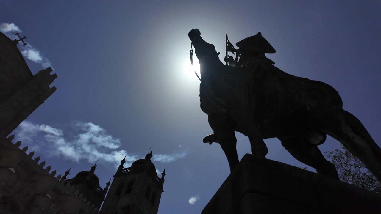 Tomada dramática em ângulo baixo da estátua equestre de Vímara Peres silhuetada contra o sol forte, com as icónicas torres da Sé do Porto e céu azul no centro histórico da cidade, classificado pela UNESCO.