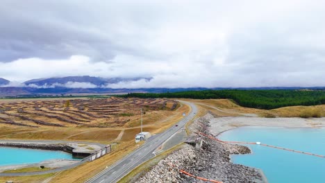 aerial view of a car driving along lake pukaki with stunning turquoise waters and mountainous backdrop under overcast skies
