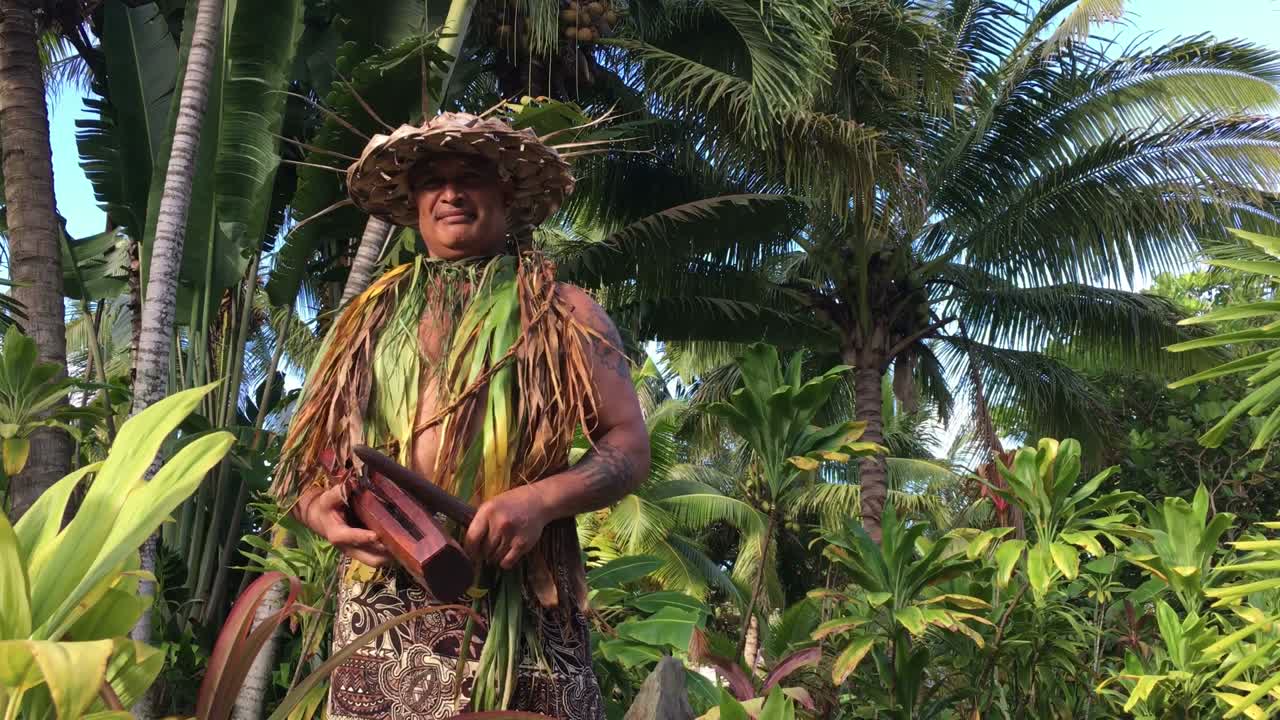 un hombre de las islas del pacífico toca un pequeño tambor de palo de madera.