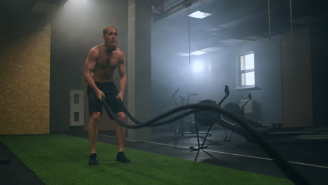 fitness man exercising with battle rope abandoned warehouse. tough man working out in cross training gym made inside old factory.