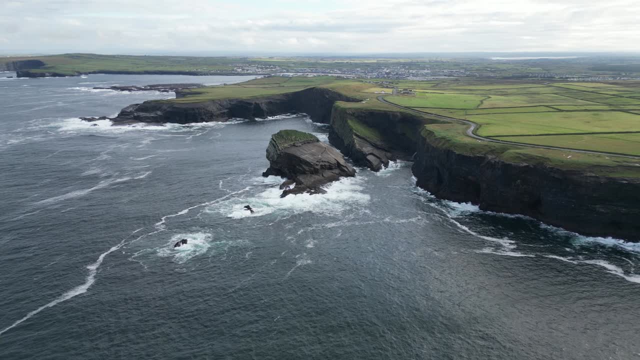 acantilados de kilkee en irlanda con olas que se estrellan contra costas rocosas, campos verdes en la distancia, vista aérea