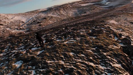 un hombre con gafas vr parado sobre el empinado acantilado de las tierras altas con finas láminas de nieve derretida en grietas rocosas en islandia - tiro de rotación de drones