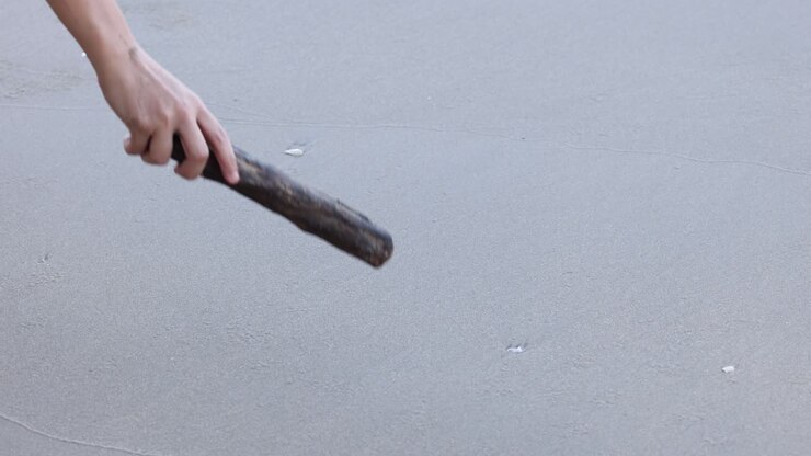 Hand drawing a heart with a stick in sand