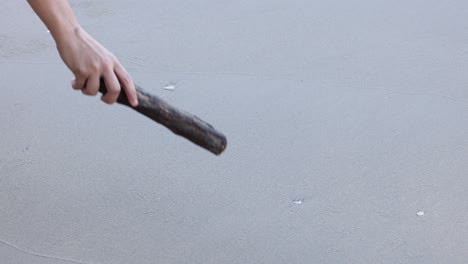 mano dibujando un corazón con un palo en la arena