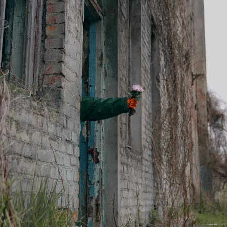Hand with fresh flowers in abandoned place. Abandoned place after chemical attack. Human&#039;s hand in protective glove hold flowers. Ecological disaster