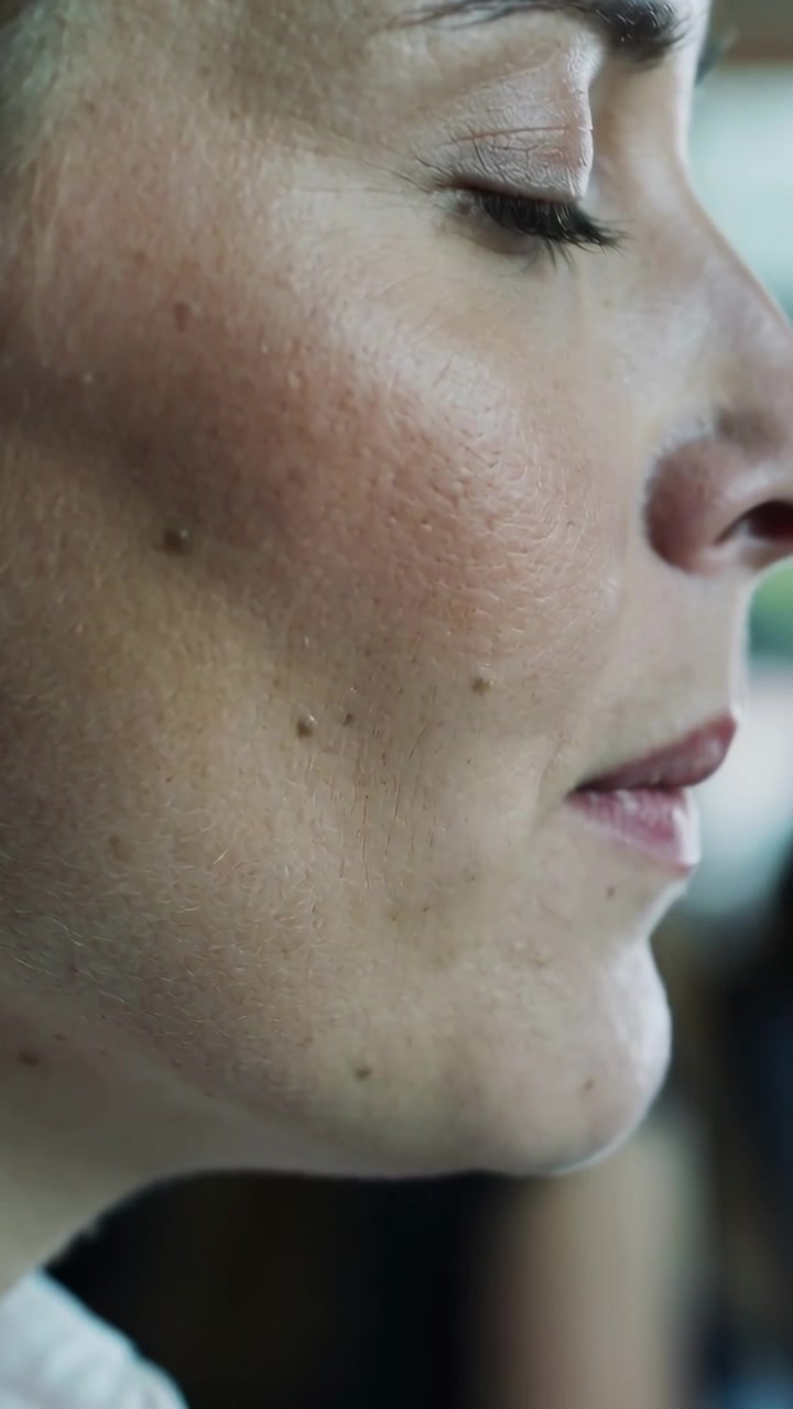 Video verticale: Donna che inspira, chiude gli occhi, separa le labbra e versa una lacrima in una piccola stanza, con nei.