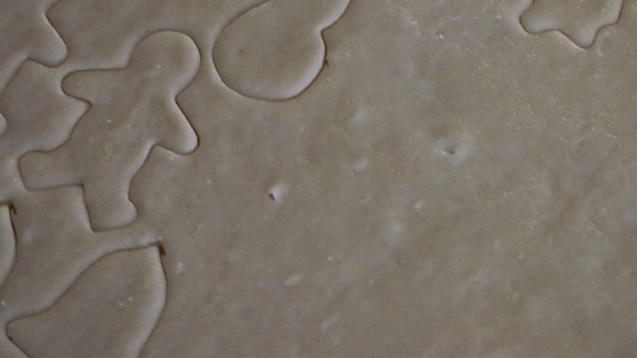 A close up of a small cookie in the shape of a girl being cut out of a sheet of cookie dough for Christmas cookies