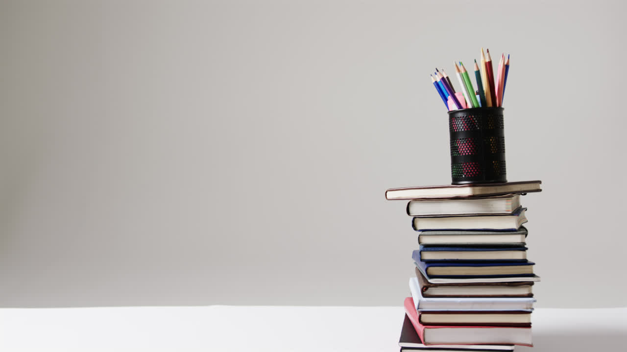 cerca de la pila de libros con lápices de colores en la taza con espacio de copia en fondo gris, en cámara lenta