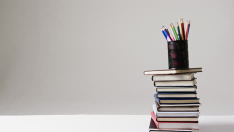 close up of stack of books with crayons in cup with copy space on grey background, in slow motion