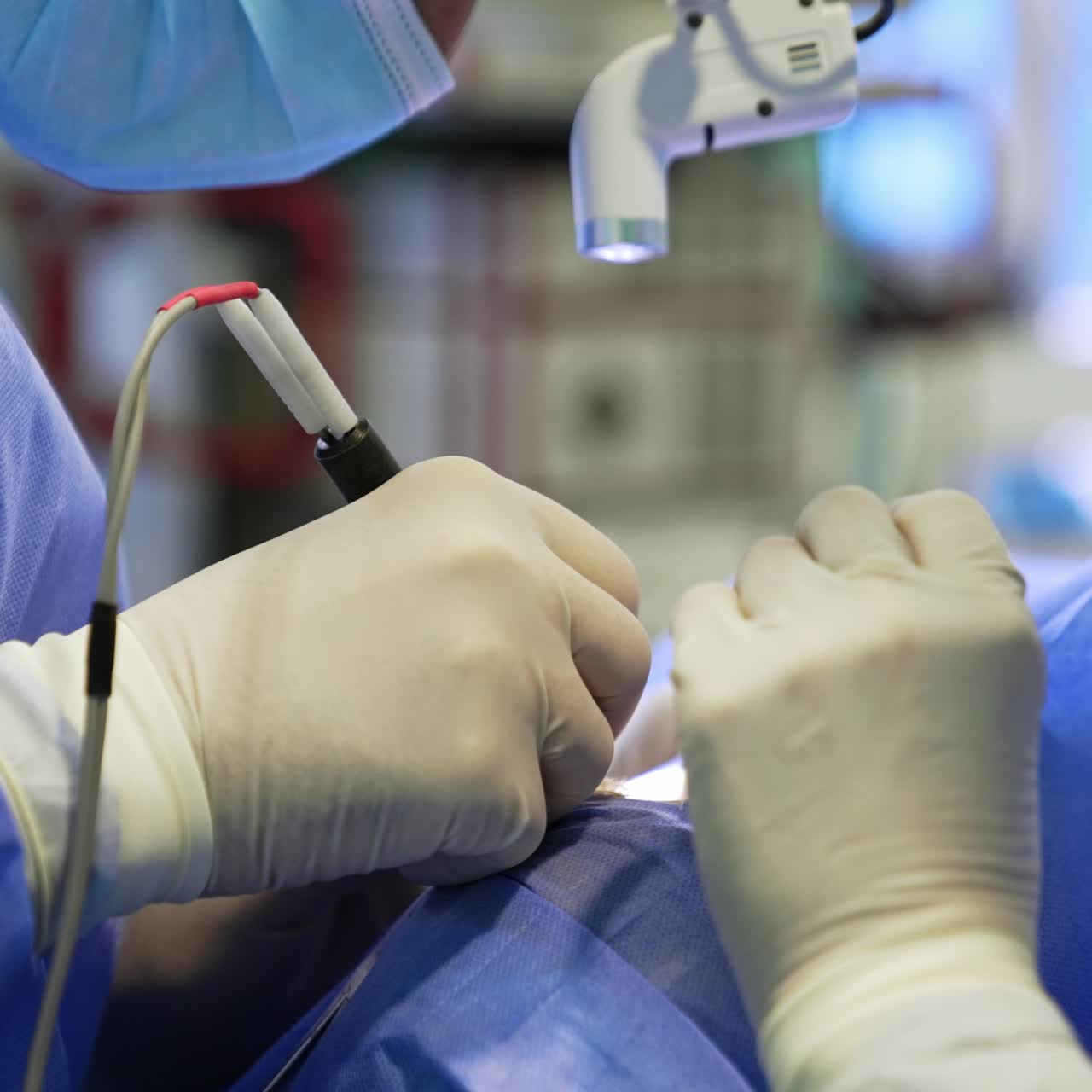 Gloved hands of two surgeons at operation. One surgeon uses electric device. Other one applies sponge. Close up