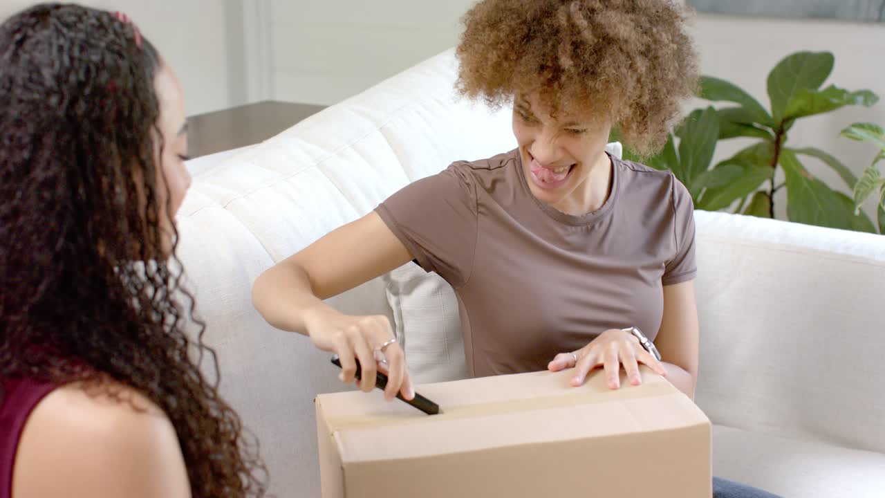 Afrikaans-Amerikaanse vrouwen kijken toe terwijl een vrouw thuis een gesloten doos opensnijdt en een cadeau tevoorschijn komt.