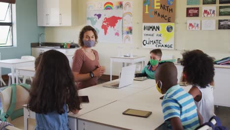 maestra que usa una máscara para la cara enseñando a los niños en la clase en la escuela