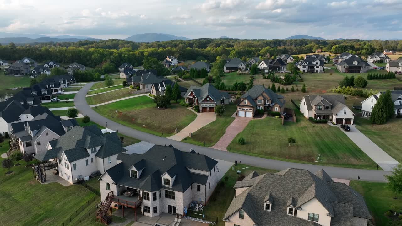 Quartiere residenziale americano di periferia con case unifamiliari indipendenti, tetti a due falde, facciate in mattoni, vialetti ampi e giardini ben curati lungo una strada curvilinea. Ripresa aerea in avvicinamento. Quartiere signorile