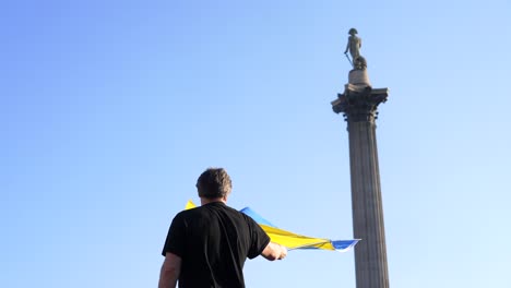 london stands with ukraine, protester waving the ukrainian flag in trafalgar square in london during protest against war with russia