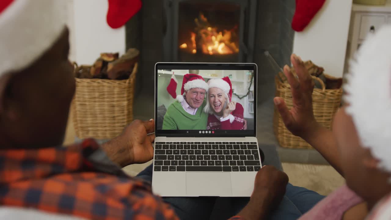 pareja afroamericana con sombreros de santa usando una computadora portátil para una videollamada de navidad con la pareja en la pantalla