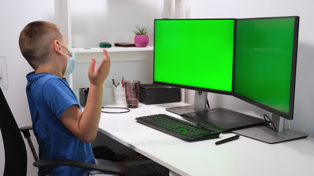 Child boy studying homework against two green monitors or screens during online lesson at home. E-learning, webinar. Online distance education for children caused by coronavirus pandemia quarantine