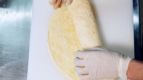 cook is wrapping pita with filling. hands of a chef in gloves cooking tasty pita with fresh vegetables. process of making tasty snack in fast food restaurant. close-up