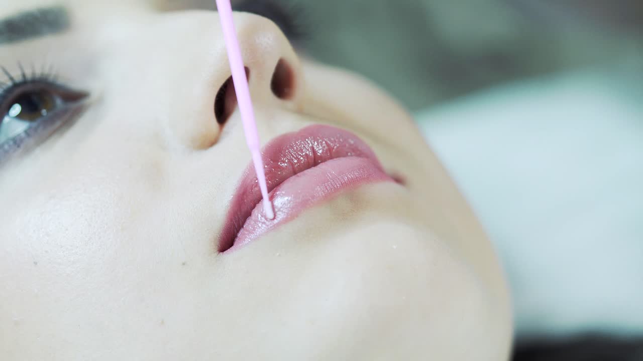 Applying red permanent make up tattoo on young girl lips. Close-up. Plastic medicine and cosmetology