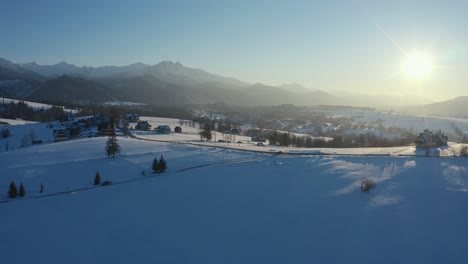 Toma-Aérea-De-Un-Dron-Con-Sol-De-Invierno-De-Una-Ciudad-Tranquila-Con-Un-Coche-Pasando