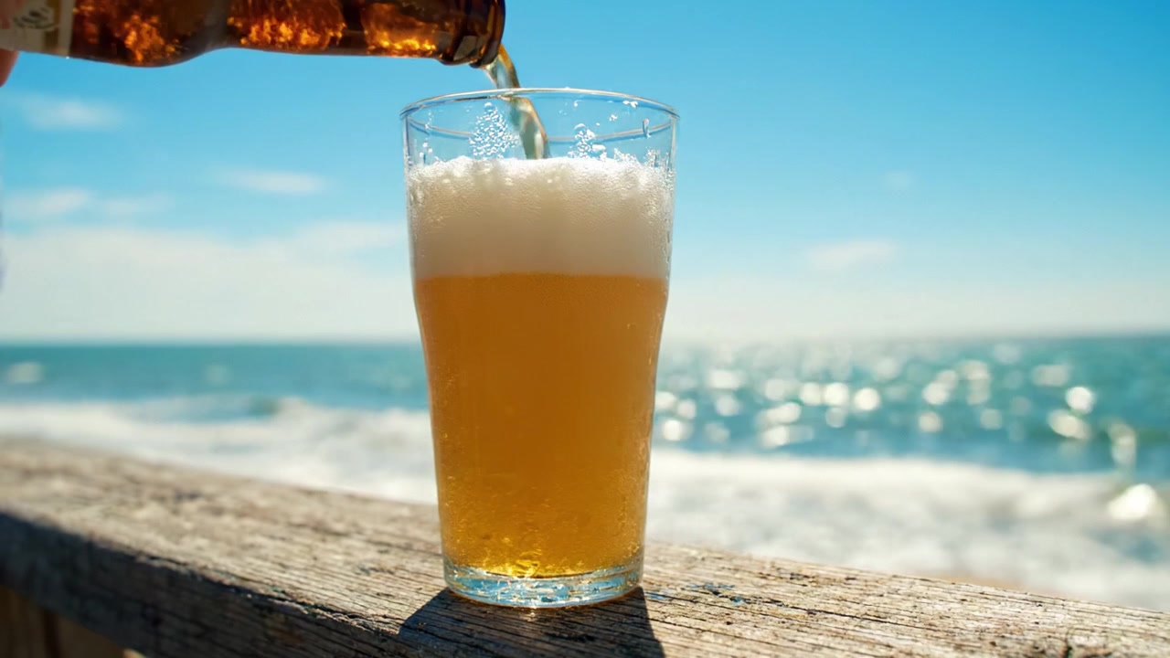 Un rinfrescante bicchiere di birra attende in riva al mare: Godersi le onde, il sole e i panorami del tramonto con una bevanda fredda in una splendida giornata sull'oceano