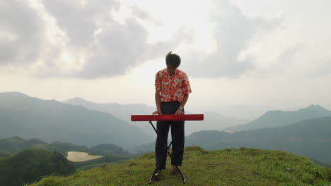 Asian-guy-playing-keyboard-at-mountain-in-Vietnam,-handheld-moving-forward