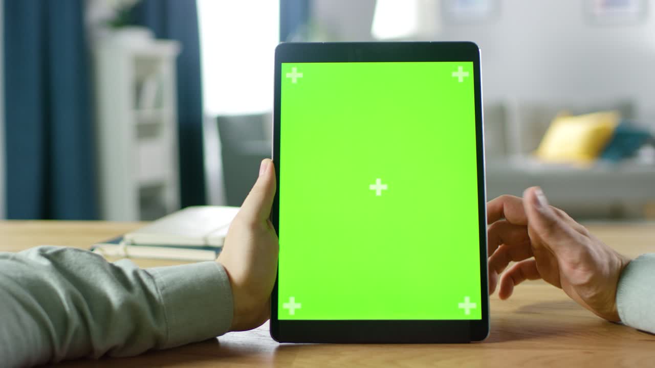 primer plano de un hombre usando una pantalla de maqueta verde, una tableta digital en modo retrato mientras está sentado en su escritorio. en el fondo, una acogedora sala de estar.