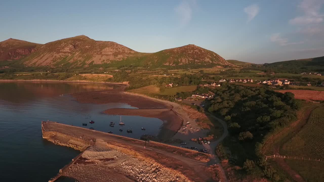 Vista aerea in discesa della baia di Trefor con lo sfondo dei monti di Snowdonia, cieli azzurri in una giornata estiva, sul Mare d'Irlanda nella penisola di Llŷn nel Galles del Nord