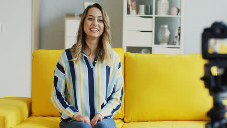 feliz bloguera grabando un video para sus seguidores sentada en un sofá amarillo en casa 2
