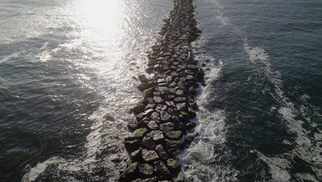 Aerial-drone-fly-over-channel-marker-and-rocky-jetty-with-lens-flare