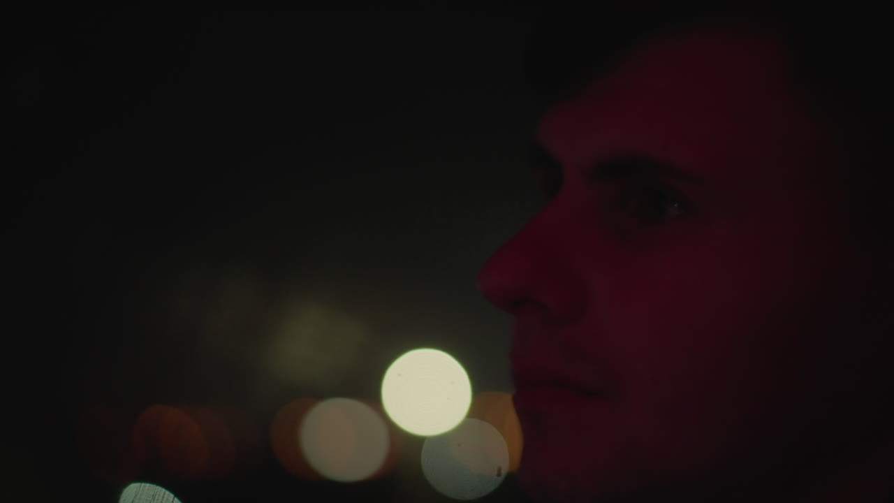 Contemplative driver in vehicle at night, Silent journey through city under soft red glow, Solitary driver with thoughtful expression navigating city streets under subdued lighting conditions