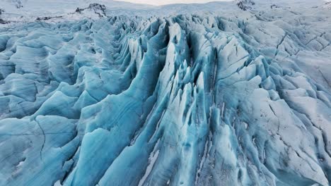 aerial view over textured ice formations of a glacier in iceland, at sunset