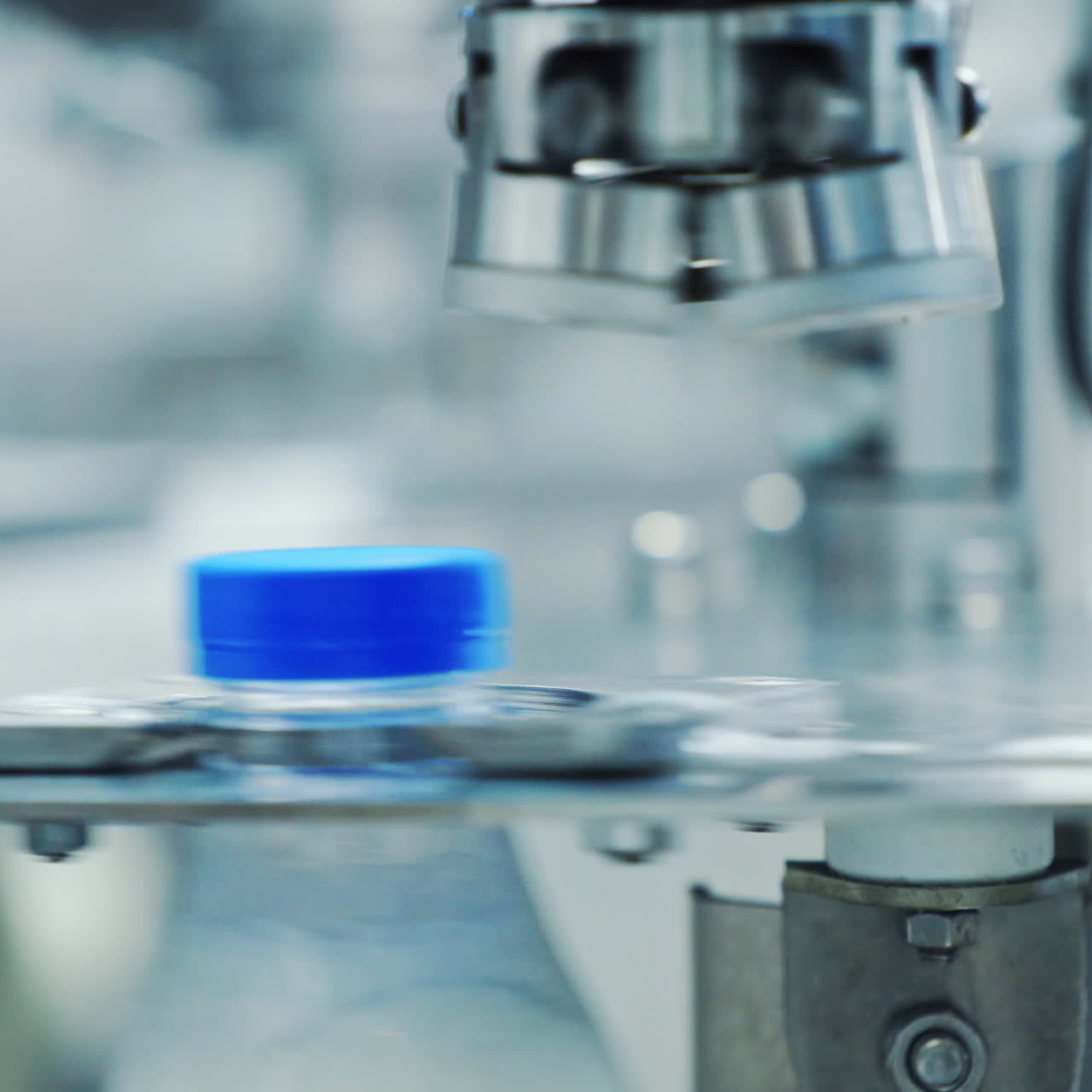 Robotic machine of twisting lid on a plastic bottle. Automated process of putting cover on a bottle with milk in a modernized diary plant. Close-up.