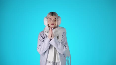 young blonde woman wearing winter clothes, feeling cold, colorful studio portrait