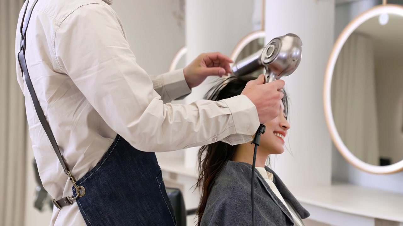 Hairdresser stylist drying and styling woman long dark hair using round brush and professional hairdryer to style hair, perfect haircut, hairstyle beauty treatment awaits for clients in modern salon
