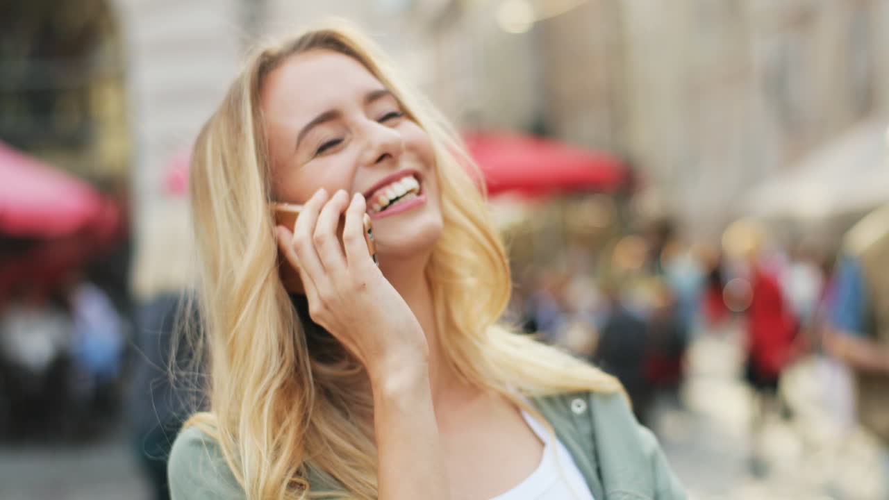 vista de cerca de una mujer rubia caucásica hablando por teléfono inteligente y riéndose en la calle