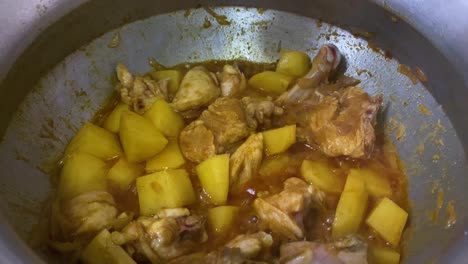 curry de pollo burbujeante con papas cortadas en cubitos cocinando en una olla grande y agregando aceite