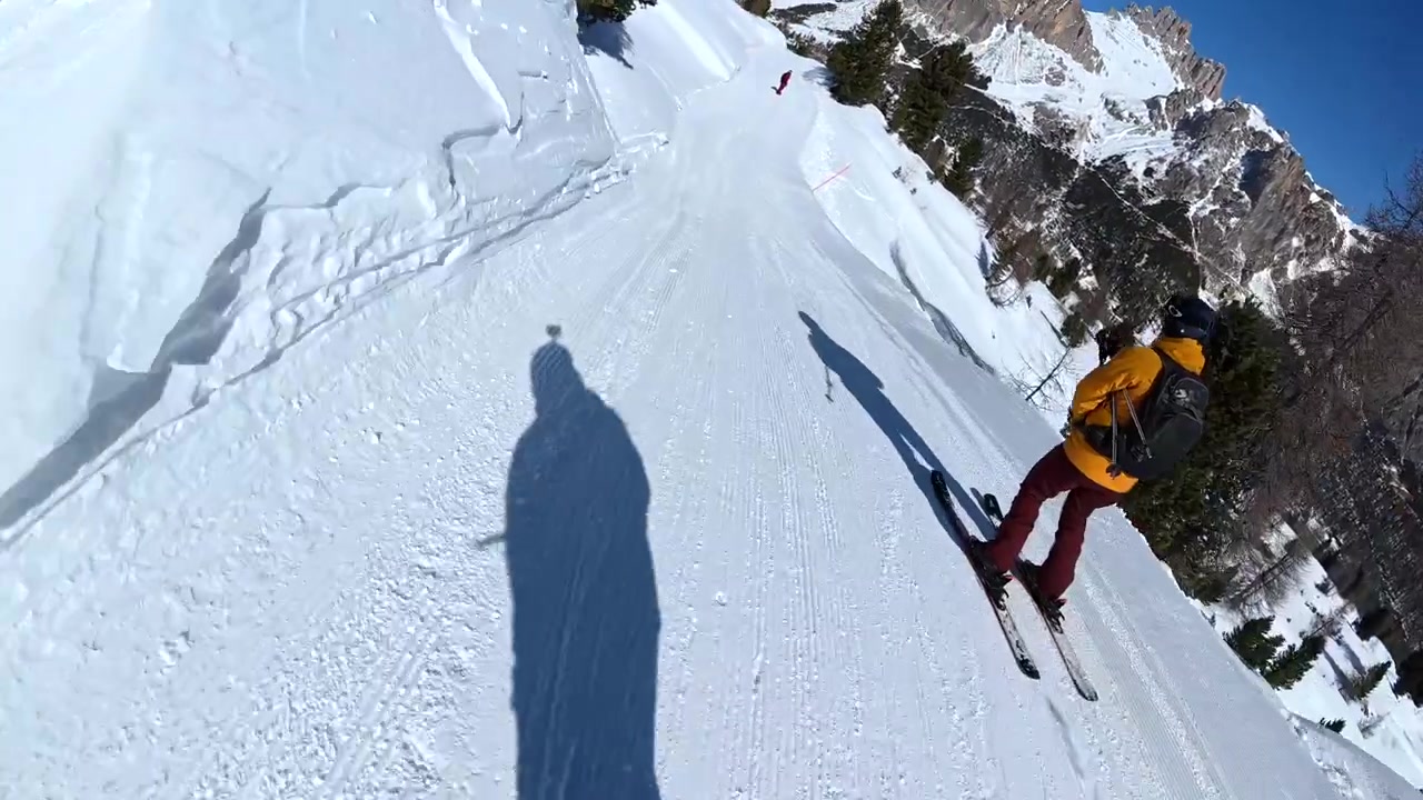 Snowboarder che segue uno sciatore giù per una pista da sci battuta