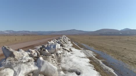 aerial view of dirt road with snow melting in field