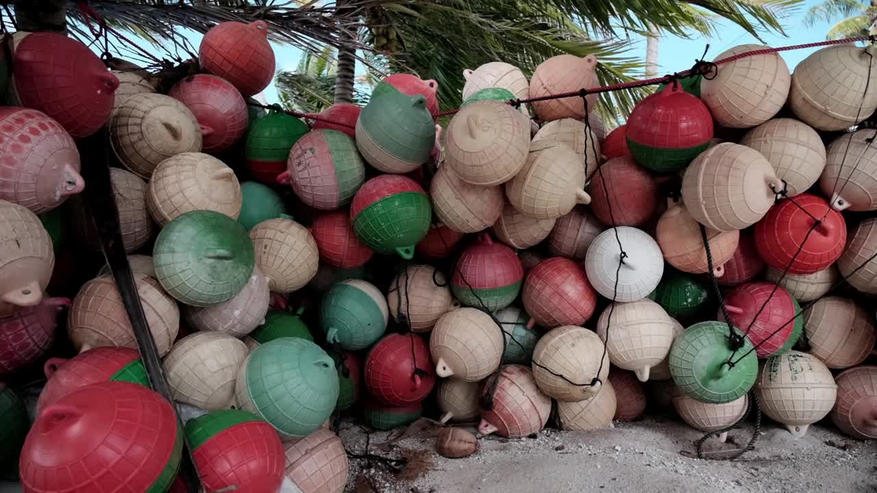 una enorme pila de boyas de pesca de plástico coloridas apiladas bajo algunas palmeras en una isla tropical para ser utilizadas para la pesca con redes