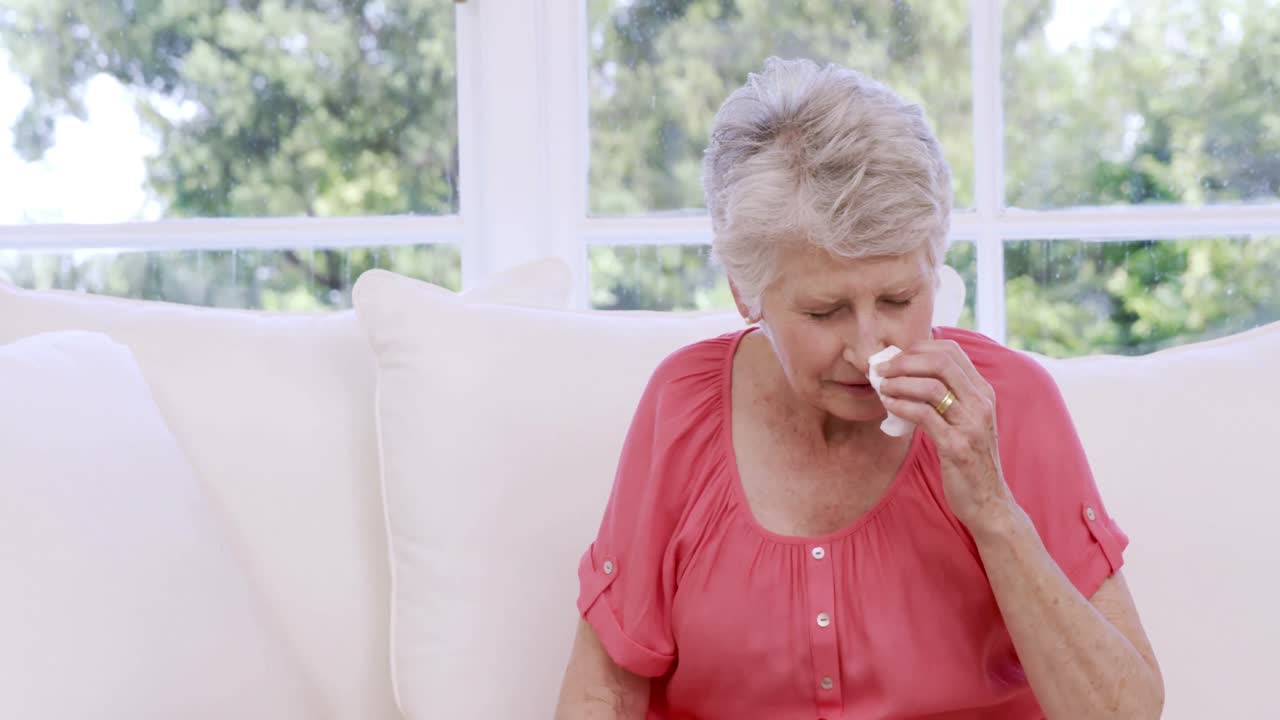 una mujer mayor estornudando en el sofá.